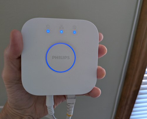 A person holding a powered Philips Hue Bridge with blue status lights.